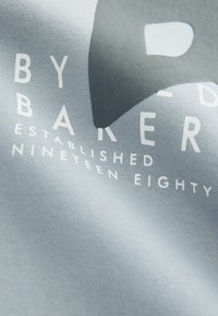 Gray cotton fabric featuring white text "BY BAKER ESTABLISHED NINETEEN EIGHTY" with a smooth texture and subtle sheen.