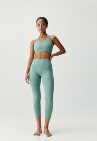 Jasnozielony stanik sportowy z krzyżującym się wzorem i dopasowanymi legginsami z wysokim stanem. Gładki, elastyczny materiał, długość do kostek.