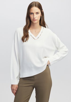 Sweater blanc en tricot avec un col en V, des épaules tombantes et un ourlet côtelé. Associé à un pantalon ajusté vert olive. Design simple, texture légère.