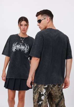 Black oversized t-shirts with a distressed finish and white graphic print. Worn with a pleated black skirt and camouflage pants.
