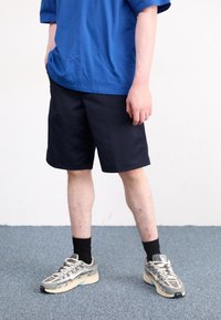 Blue short-sleeve t-shirt and navy shorts. Feet in gray running shoes with black socks. Smooth fabric, relaxed fit, and knee-length shorts.