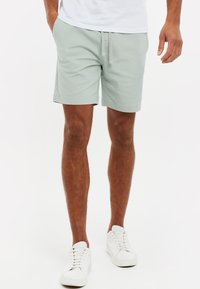 Lys grønne shorts lavet af blødt stof med en snor i taljen, rullede kanter og sidelommer. Sættes sammen med hvide sneakers.
