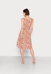 Vestido floral sem mangas em tons de vermelho, rosa e amarelo, com um corpete ajustado e saia esvoaçante, combinado com sandálias de tiras rosa claro.