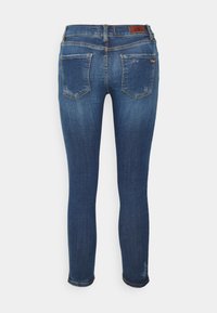 Jeans ajustados en denim azul oscuro. Presentan una cintura de altura media, bolsillos traseros, un ligero desgaste y costuras en contraste a lo largo de las costuras.