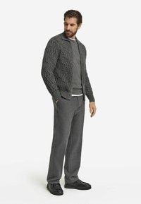 Szary dzianinowy kardigan z fakturowanym wzorem, nakładany na szarą bluzę, zestawiony z szarymi spodniami i czarnymi trampkami.