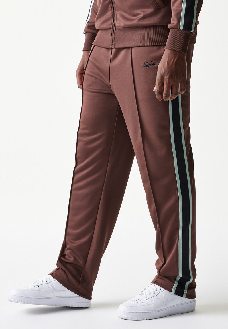 Καφέ αθλητικό παντελόνι από λείο ύφασμα, με πλευρικές ρίγες σε τιρκουάζ και μαύρο. Διαθέτει εφαρμοστή γραμμή και ελαστική μέση. Συνδυάζεται με λευκά αθλητικά παπούτσια.