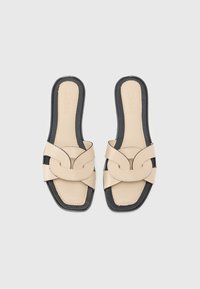 Béžové kožené nazouvací sandály s černou podrážkou, s překříženým páskem a čtvercovou špičkou. Hladká textura s kontrastním prošíváním.