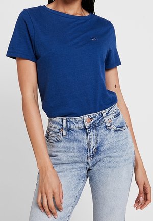 Kvinde iført en ensfarvet blå kortærmet t-shirt stoppet ned i lyseblå højtaljede cowboybukser.