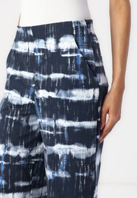 Marineblauwe gebloemde broek met abstracte penseelstreekontwerpen in wit en lichtblauw. De stof heeft een soepele textuur en een ontspannen pasvorm.