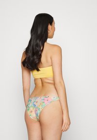 Top bandeau amarelo com textura canelada e parte de baixo de biquíni floral em tons pastéis, apresentando cores verde, rosa e azul com uma textura suave.