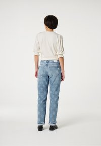 Lichtbeige top met pofmouwen, gecombineerd met lichtblauwe hoge taille jeans met een bloemenpatroon. Zwarte schoenen maken de outfit compleet.