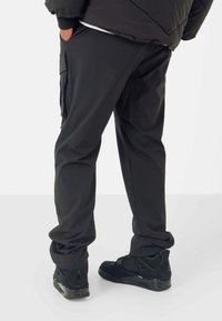 Zwarte cargobroek met zijzakken en een losse pasvorm, gecombineerd met zwarte sneakers met gaasdetails en een gestructureerde zool.