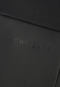 Borsa in tessuto nero con superficie testurizzata, logo "JOOP JEANS" in rilievo e design elegante e minimalista, privo di accessori o dettagli aggiuntivi.