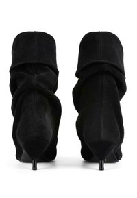 Mustadest sametist pahkluu saapad, millel on lahtine disain, teravad varbad ja stilettokontsad, ning pahkluu ümber keeratud äär.