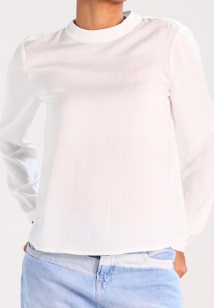 Witte lange mouw top met een ronde hals, zachte textuur, verlaagde schouders en rechte zoom, gecombineerd met lichtblauwe jeans.