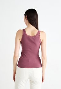 Top a canotta a coste color malva con pizzo lungo il colletto e le spalline, caratterizzato da un design aderente e una leggera curvatura all'orlo.