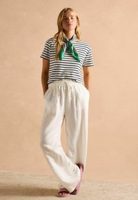 Ribidega T-särk lühikeste varrukatega, millele on lisatud laiad valged linased püksid ja roosad sandaalid. Kaelal on rohelise bandaanaga lips.