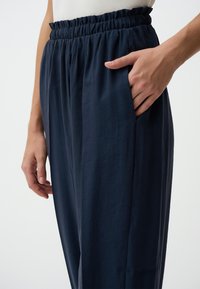 Marineblauwe wijde broek met een verzamelde, elastische tailleband. Heeft zijzakken en een lichtgewicht, gestructureerde stof.