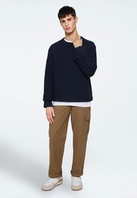 Marine gebreide trui met een textuurpatroon, gecombineerd met lichtbruine cargo pantalons met zijzakken en witte sneakers.