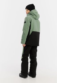 Groene en zwarte waterdichte jas met capuchon, met een kleurblokontwerp, gestructureerde stof en elastische manchetten, gecombineerd met zwarte broek.
