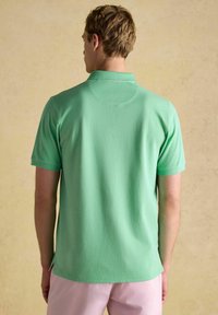 Piparmētru zaļš polo krekls ar īsām piedurknēm, ar klasisku apkakli un taisnu apakšmalu, izgatavots no mīksta kokvilnas materiāla.