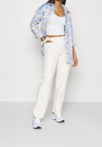 Jasnoniebieska i beżowa wzorzysta polarowa kurtka, biała krótka bluzka, kremowe szerokie spodnie z bocznymi wycięciami oraz białe buty sportowe.