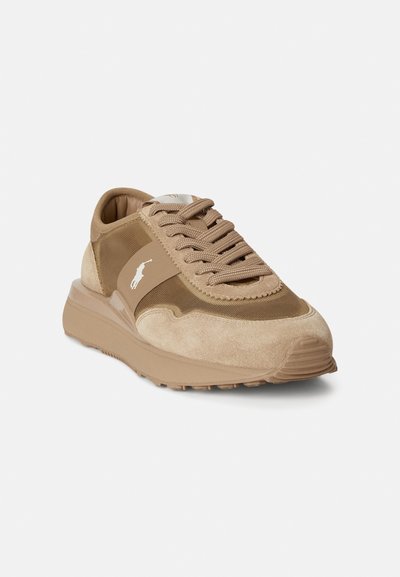 Μπεζ αθλητικά παπούτσια με συνδυασμό σουέντ και υφασμάτινων υλικών, στρογγυλεμένη μύτη, μαλακό επάνω μέρος στον αστράγαλο και υφασμένο πέλμα με εμφανές λογότυπο.