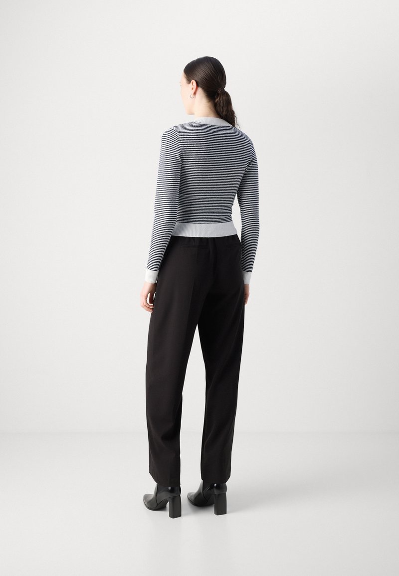 Pull en tricot rayé bleu et blanc, au design court avec des poignets et un ourlet côtelés, porté avec un pantalon noir et des bottes à talons noires.