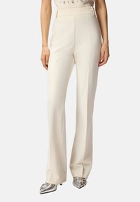 Pantaloni bianchi a vita alta con una vestibilità sagomata, caratterizzati da una texture liscia e dettagli a piega frontale. Abbinati a scarpe metallizzate con punta affusolata.