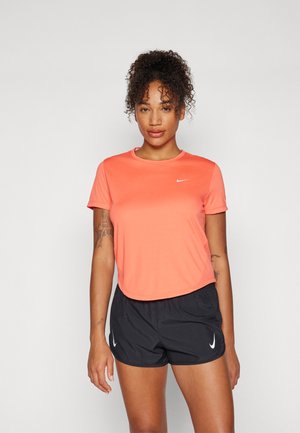 Nike Sport-T-Shirt in lebhaftem Korallrot, mit kurzen Ärmeln und rundem Ausschnitt, kombiniert mit schwarzen Shorts, die weiße Logo-Akzente haben. Weicher, elastischer Stoff.