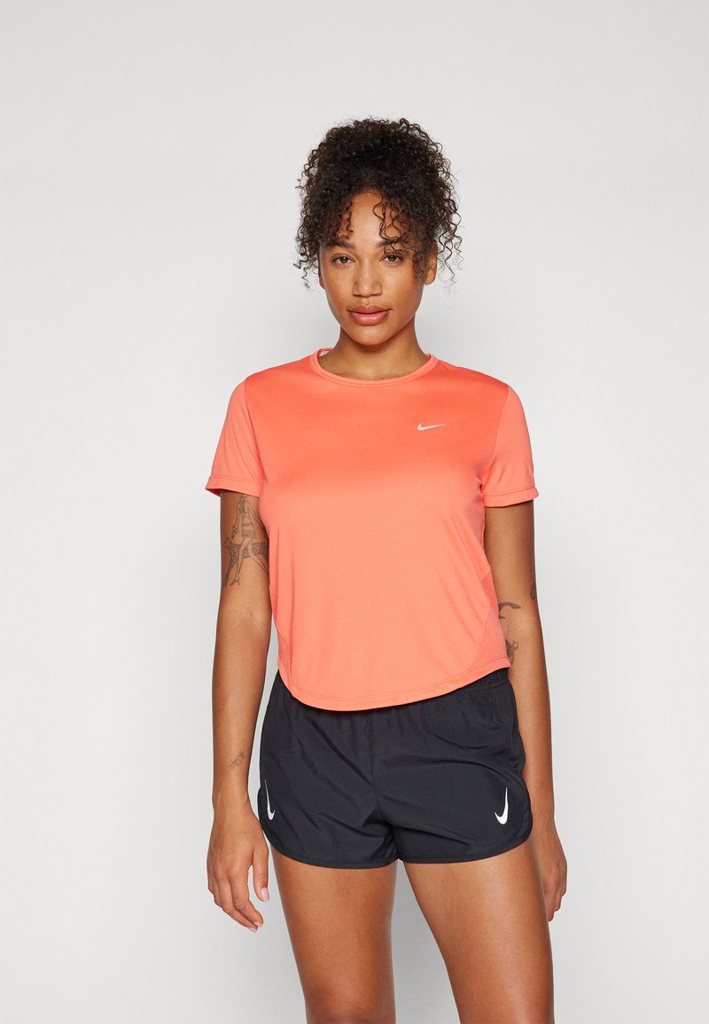 Nike atletska majica u vibrantnoj koraljnoj boji, kratkih rukava, okruglog izreza, uparena s crnim šortsevima koji imaju bijele logo akcente. Mekani, rastezljivi materijal.