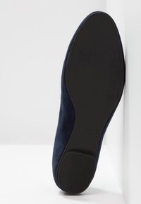 Semelle d'une chaussure plate en daim bleu foncé avec une semelle extérieure en caoutchouc noir texturé et un petit talon, taille 37 visible sur la semelle.