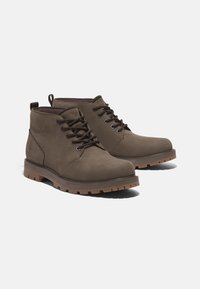 Brown leather ankle boots with round toe, contrasting rubber sole, and flat laces. Features a logo on the side and padded collar for comfort.