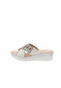 Sandal in neoprene bianco con cinturini incrociati. Presenta un accentuatura testurizzata in argento e una suola in schiuma confortevole con un leggero tacco a zeppa.