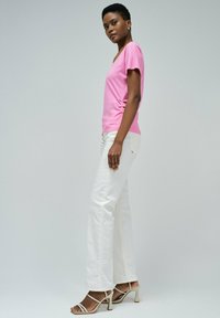 Camiseta rosa de manga corta con cuello en V, combinada con vaqueros blancos de pierna recta y tacones beige con tiras, mostrando una textura suave y un diseño ajustado.