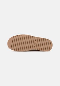 Flat shoe sole, light brown rubber with horizontal grooves for traction, rounded toe, and minimal branding imprints.