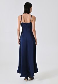 Navy satijnen maxi-jurk met verstelbare spaghetti-bandjes, een getailleerde bovenkant en een vloeiende rok. Voorzien van een ritssluiting aan de achterkant.