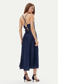 Abito midi in denim blu scuro con scollatura a V, spalline regolabili e design con lacci. Abbinato a sandali con tacco alto color navy.