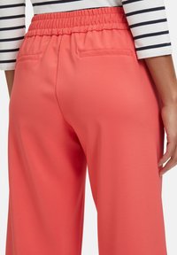 Coral wide-leg pants with a soft texture, elastic waistband, and two back pockets, featuring a smooth, matte finish and tailored seams.