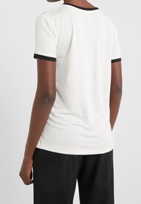 Vit bomull t-shirt med svart kontrasterande kant vid halsringningen och ärmarna; korta ärmar och en avslappnad passform. Slät textur.