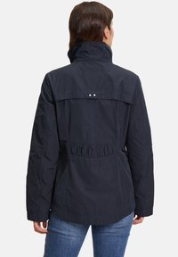 Tummansininen takki, jossa on korkea kaulus, elastinen vyötärö ja kontrastiväriset saumat. Materiaali näyttää kevyeltä ja siinä on sileä viimeistely.