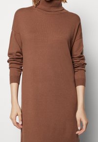 Vestito maglione a collo alto di colore marrone, con maniche lunghe, una vestibilità rilassata e una texture morbida con dettagli a coste ai polsini.