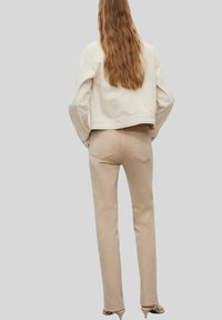 Beige denim jeans met een aansluitend design, zichtbare stiksels en achterzakken. Het model draagt een beige cropped jack met lange mouwen.