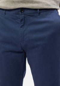 Marineblaue Chinos aus atmungsaktivem Stoff verfügen über einen Knopfverschluss, Gürtelschlaufen und eine glatte Textur sowie Seitentaschen.