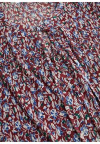Tissu rouge texturé avec imprimé floral bleu, blanc et vert, et détail de lien en tissu sur un matériau plissé.