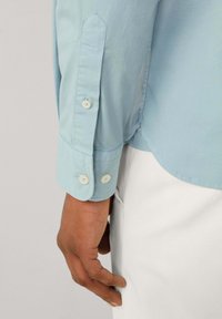 Lichtblauw lange mouwen shirt met knoopmanchetten, een gladde katoen stof en een subtiele glans, met een ronde zoom en contrasterende knopen.