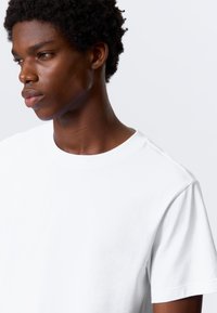 T-shirt branca de algodão com decote redondo e mangas curtas. Têxtura suave do tecido, com um corte descontraído e um design limpo.