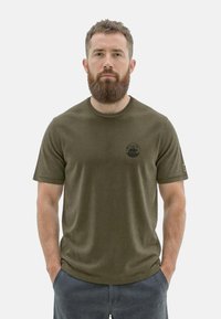 Olivgrünes T-Shirt mit kurzen Ärmeln aus weichem Stoff, mit rundem Halsausschnitt und einem kreisförmigen Logo auf der Brust.
