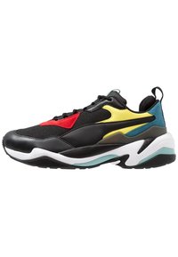 Chaussure de sport noire avec des superpositions en maille et en synthétique. Présente des accents rouges, jaunes et bleus. Semelle épaisse et blanche avec des détails en sarcelle et une adhérence texturée.