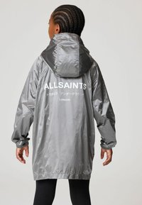 Szürke, könnyű esőkabát kapucnival, elasztikus mandzsettával, laza szabással, és fehér szöveggel a hátsó részen, amely azt írja: "ALLSAINTS LONDON."